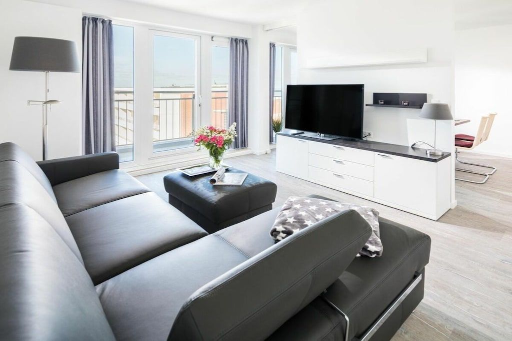 A modern living room with a sofa, a coffee table, a flat-screen TV, and a dining area with a table and chairs.