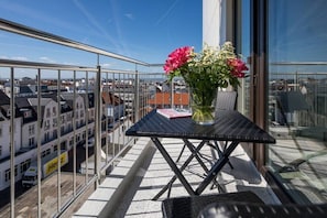 Un balcón con una mesa, un florero con flores y vistas a edificios.