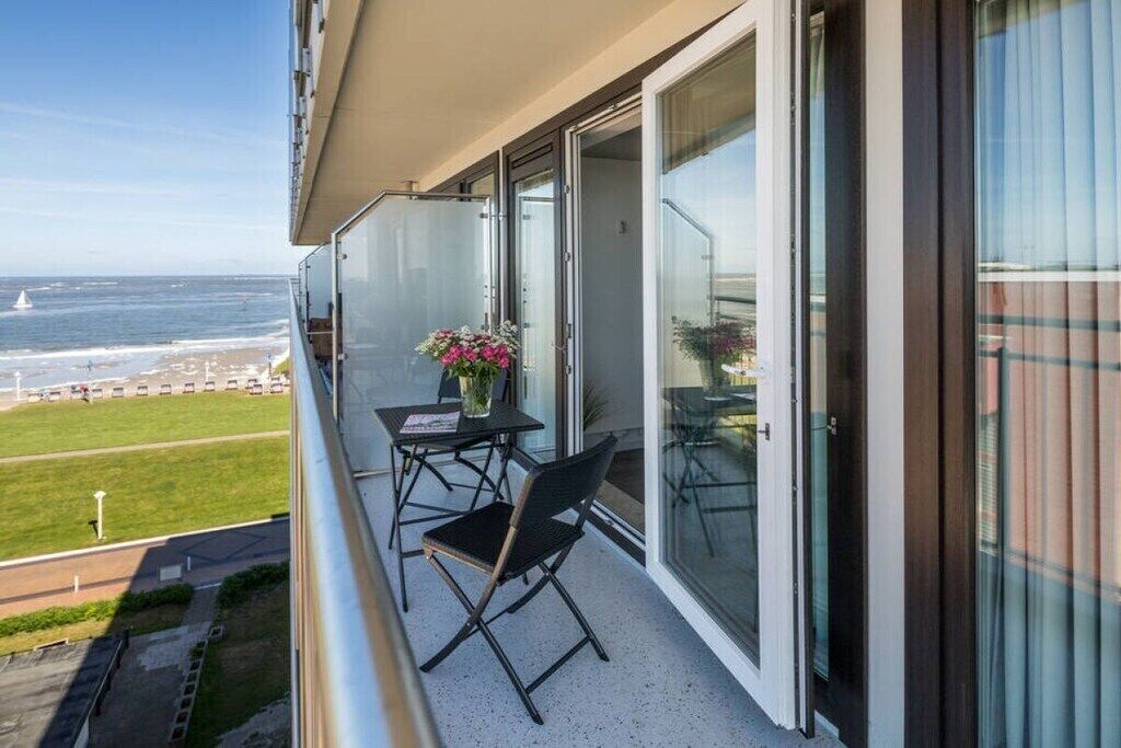 Ein Balkon mit Tisch und Stühlen mit Blick auf Strand und Parkplatz.
