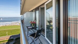 En balkon med et bord og stole, der udover en strand og en parkeringsplads.