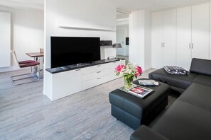 A modern living room with a flat-screen TV, a sofa, a coffee table with a magazine, and a flower vase. - Holiday apartment in Norderney with sauna (Norderney)