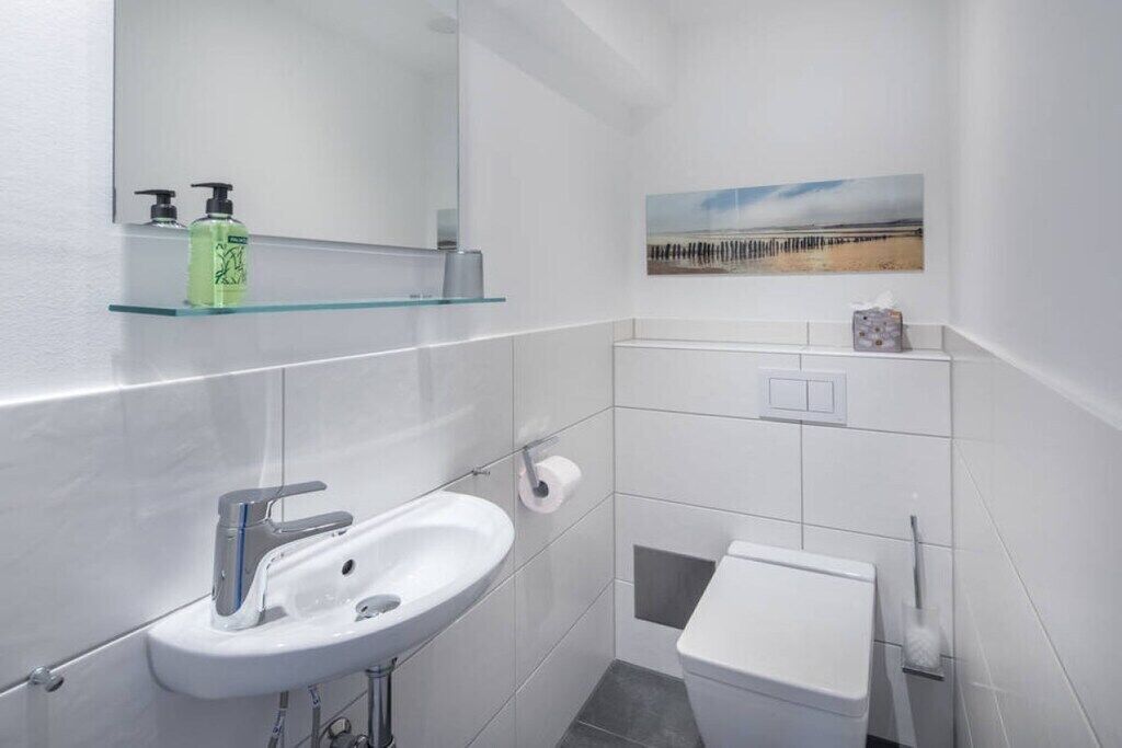Moderni kylpyhuone, jossa on valkoinen pesuallas, wc ja lasihylly, jossa on hygieniatuotteita.