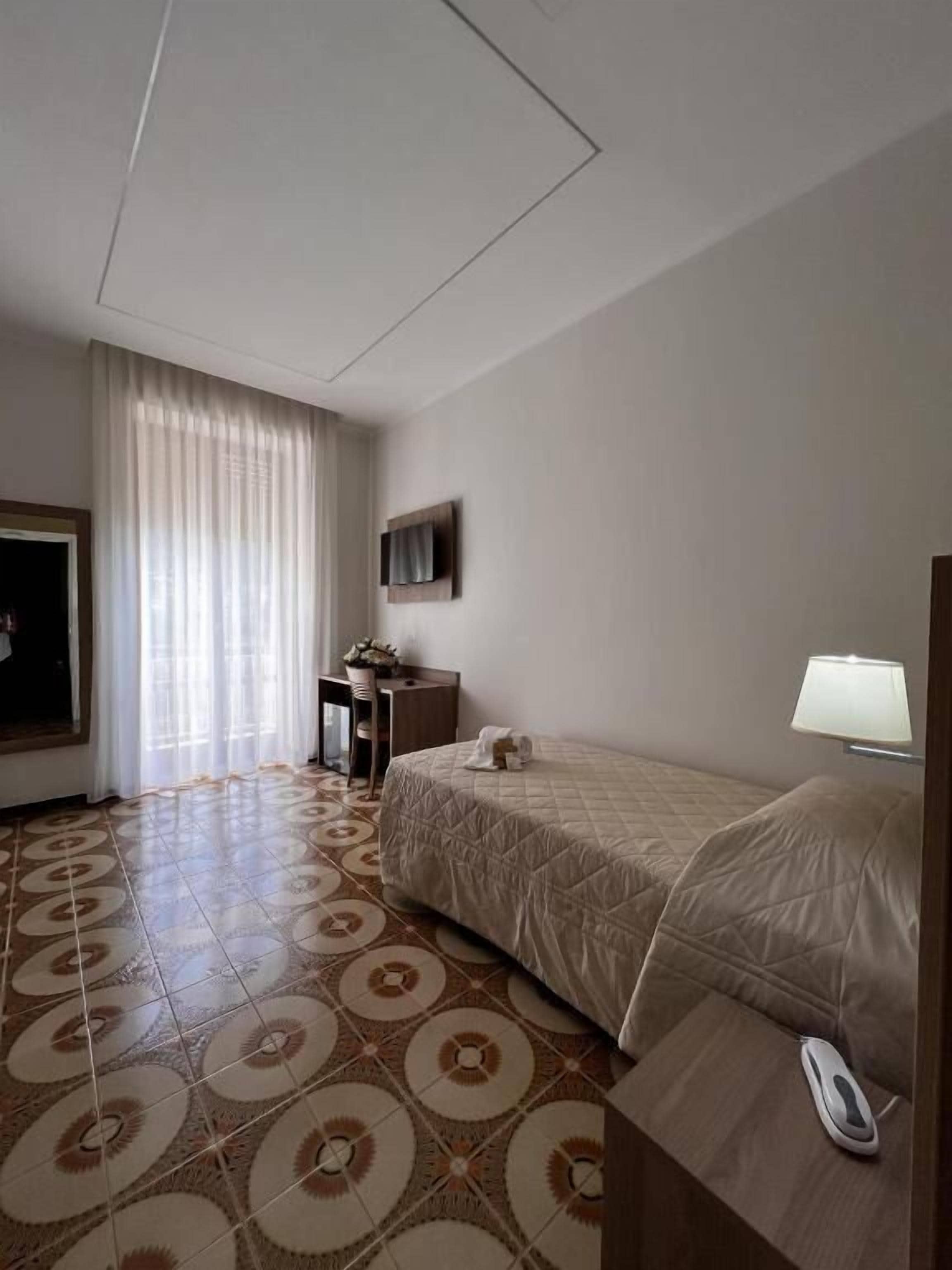 Une chambre d’hôtel avec un lit, un bureau, une chaise, une télévision et une fenêtre avec des rideaux.