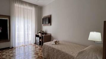 Une chambre d’hôtel avec un lit, un bureau, une chaise, une télévision et une fenêtre avec des rideaux.