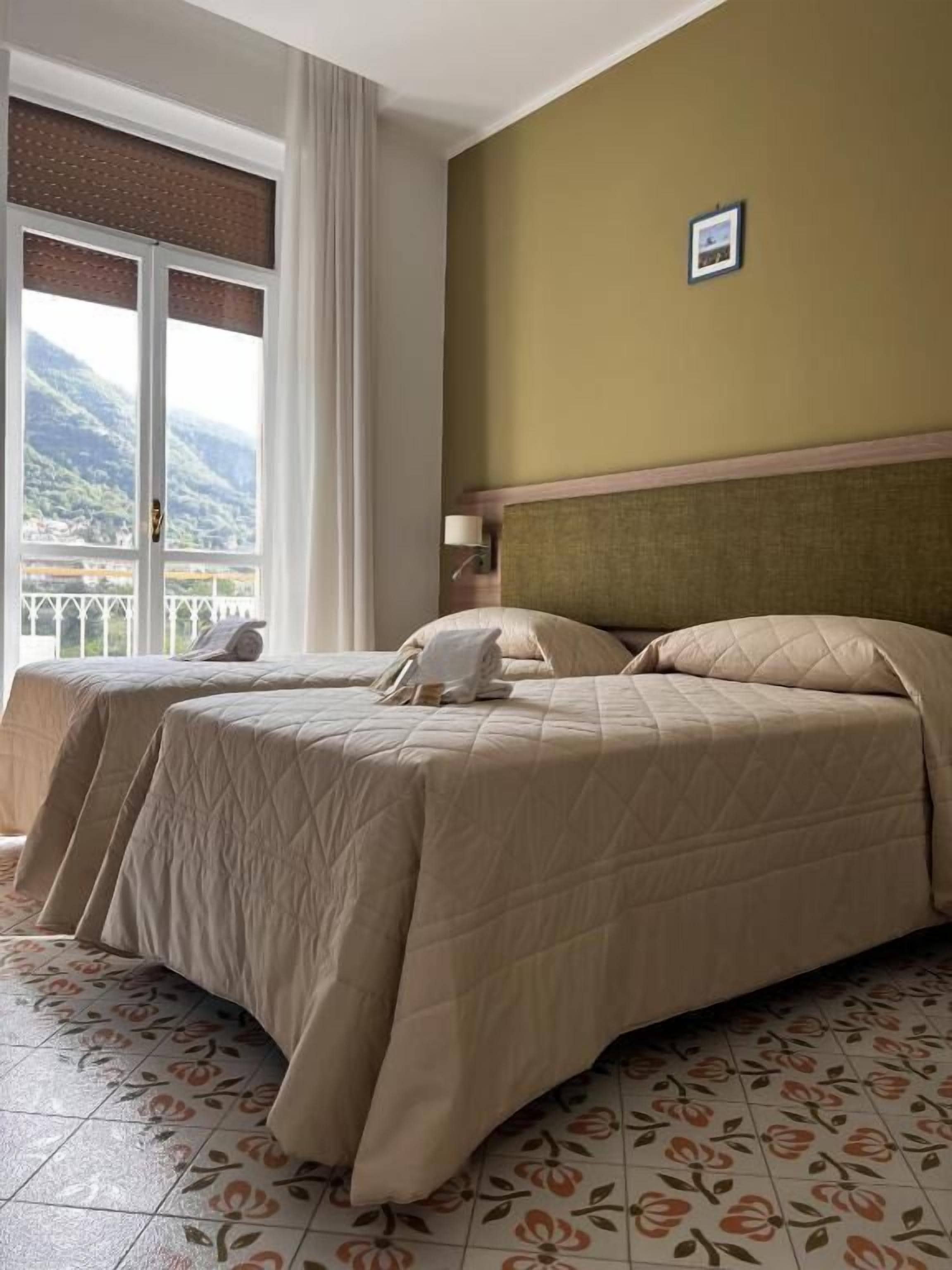 Une chambre d’hôtel avec deux lits, un balcon offrant une vue sur les montagnes et un sol orné de motifs floraux.