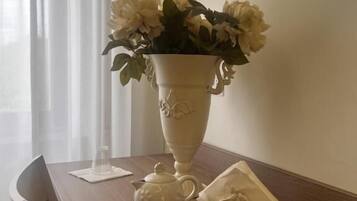Una mesa con un jarrón blanco lleno de flores, un hervidor, un control remoto y una servilleta.