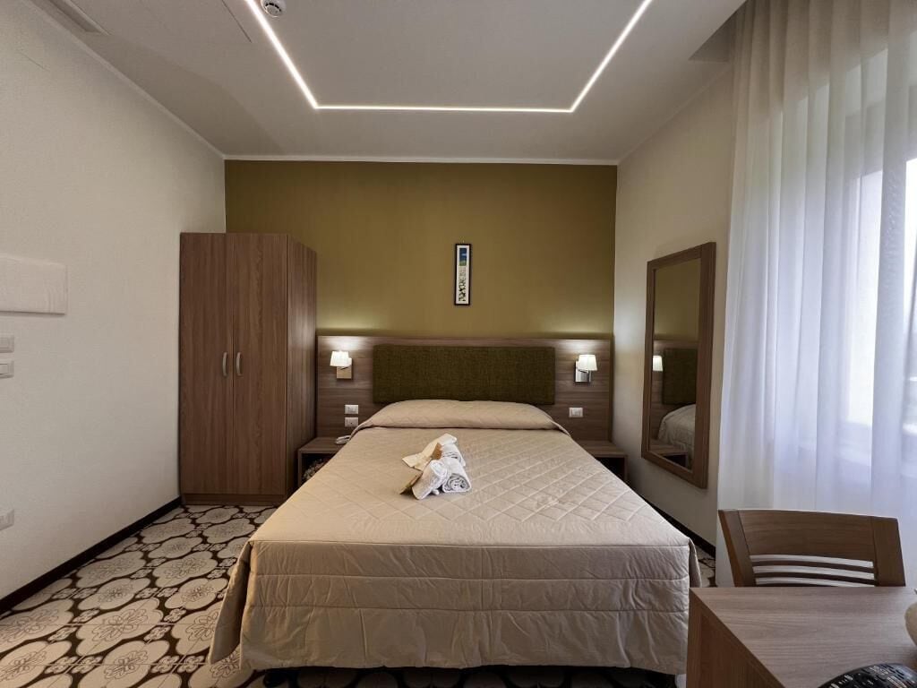 Une chambre d’hôtel comprenant un lit, une armoire en bois, un bureau avec une chaise et un miroir.
