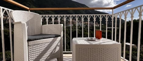 Un balcon agrémenté de meubles en osier, d’une table ronde et offrant une vue sur un paysage montagneux.