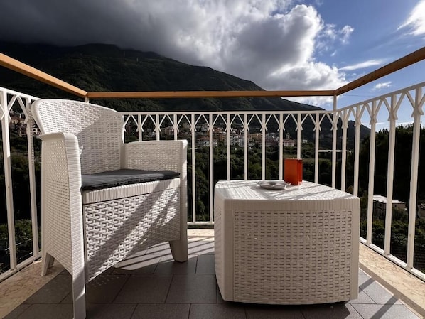 Un balcon agrémenté de meubles en osier, d’une table ronde et offrant une vue sur un paysage montagneux.