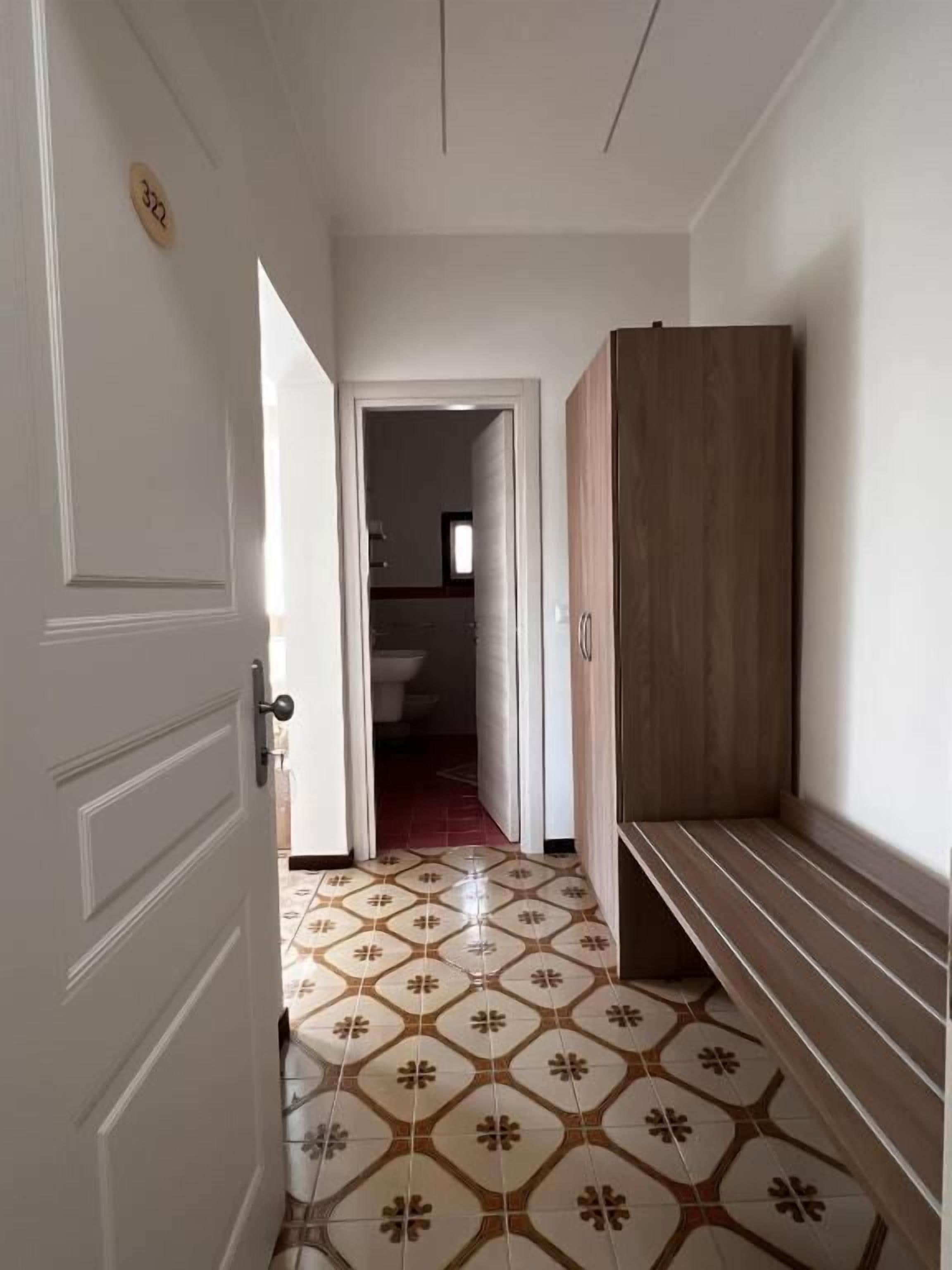A hallway with patterned flooring, a wooden wardrobe, and a door leading to another room.
