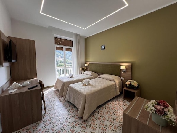 A hotel room with two beds, a desk, a television, and a window with a view.