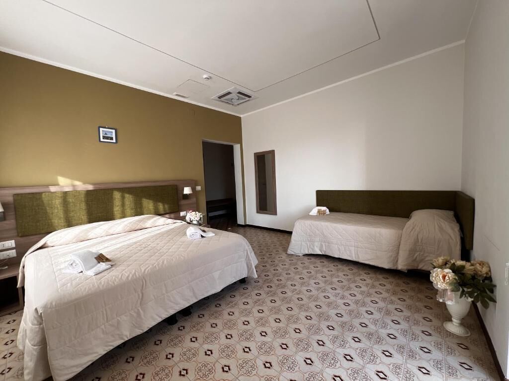 A hotel room with two beds, a large mirror, and a vase with flowers.