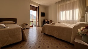 Quarto de hotel com duas camas, televisão, varanda e vista para as montanhas.