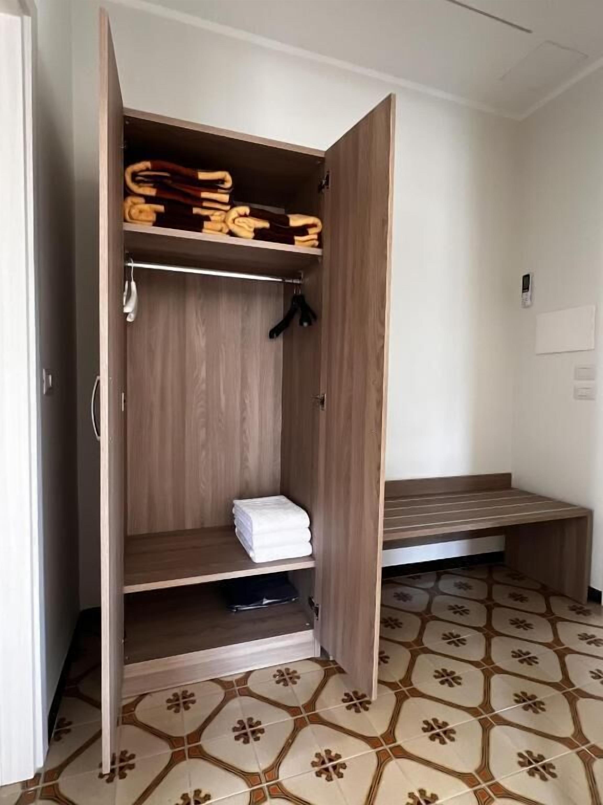 Un armario de madera con estantes y espacio para colgar, un banco y un suelo de baldosas.