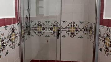 Cabina de ducha con paredes de vidrio, cabezal de ducha y panel de control.