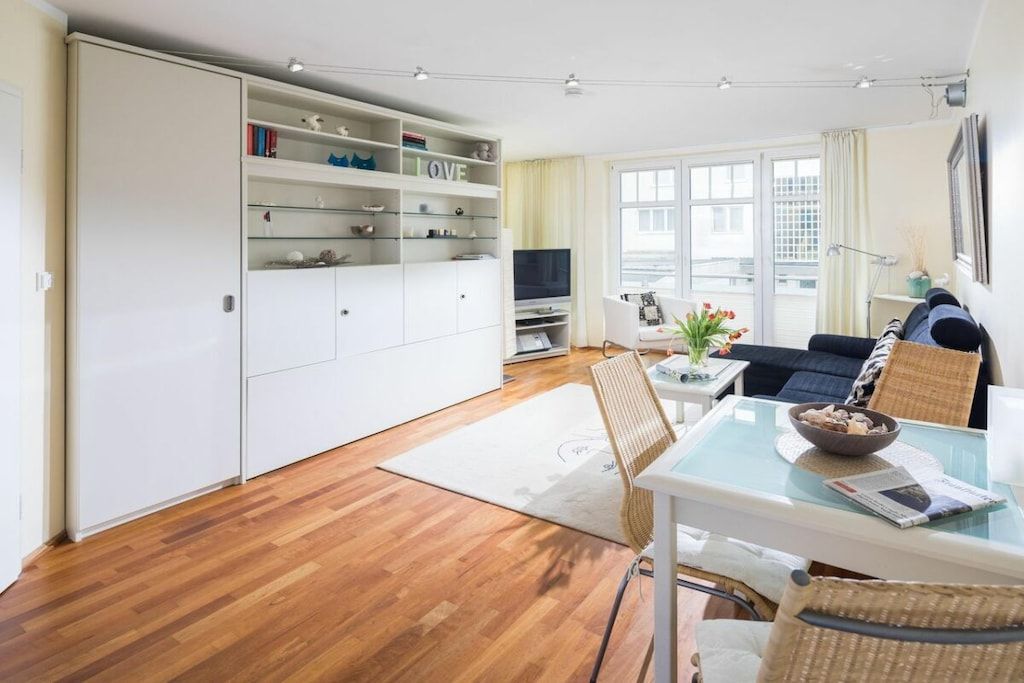 Una sala de estar moderna con un sofá, una mesa de comedor con sillas, un televisor y un mueble blanco grande con estantes.