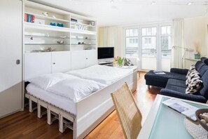 Um espaço de estar compacto com cama, sofá, televisão e estante.