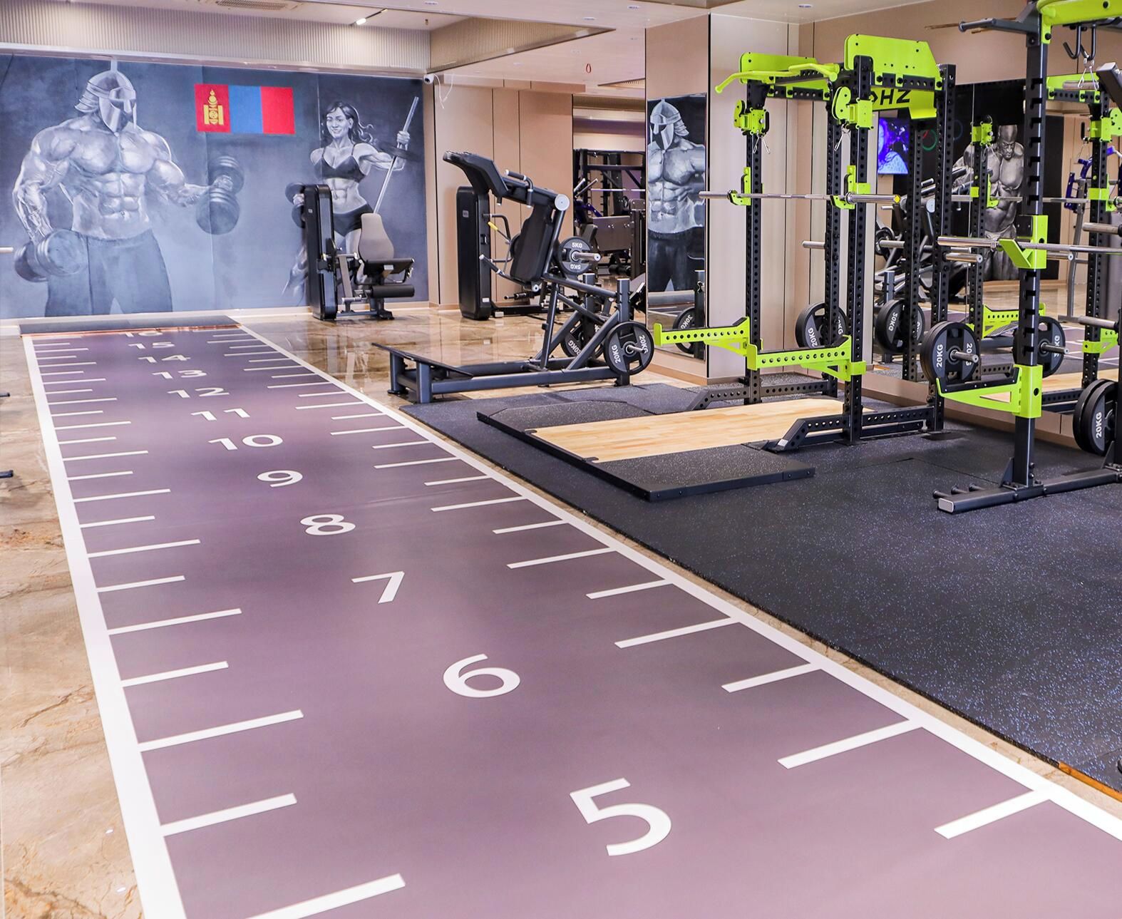Academia com equipamentos de musculação, pista de corrida e cartazes motivacionais nas paredes.