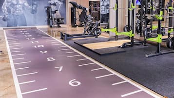 Academia com equipamentos de musculação, pista de corrida e cartazes motivacionais nas paredes.