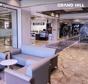 Vestíbulo del Grand Hill Center con mostrador de recepción, zona de estar y equipo de ejercicio.