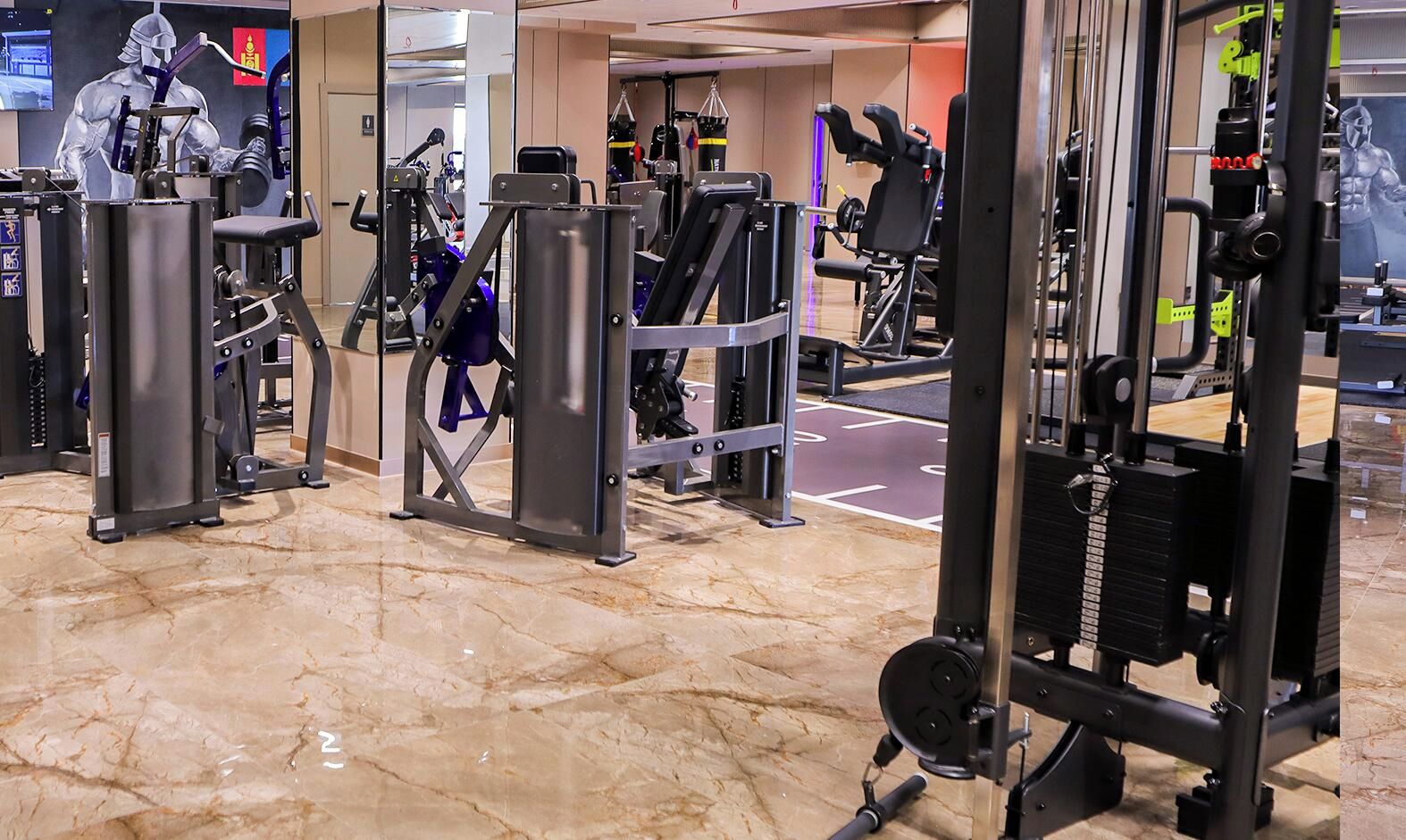 Un gimnasio con diferentes máquinas de ejercicio, suelo de mármol y un espejo grande.