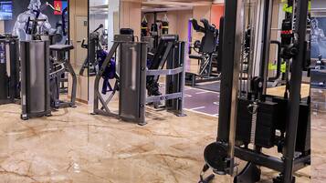 Academia com diversos equipamentos de exercício, piso de mármore e um espelho grande.