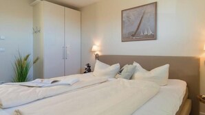 A hotel room with a bed, a wardrobe, a wall-mounted lamp, and a painting. - Holiday apartment with 1 bedroom (Heiligenhafen)