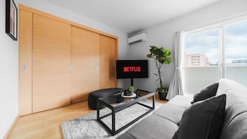 A modern living room with a sliding wooden closet, a flat-screen TV, a black coffee table, a grey sofa, and a potted plant.