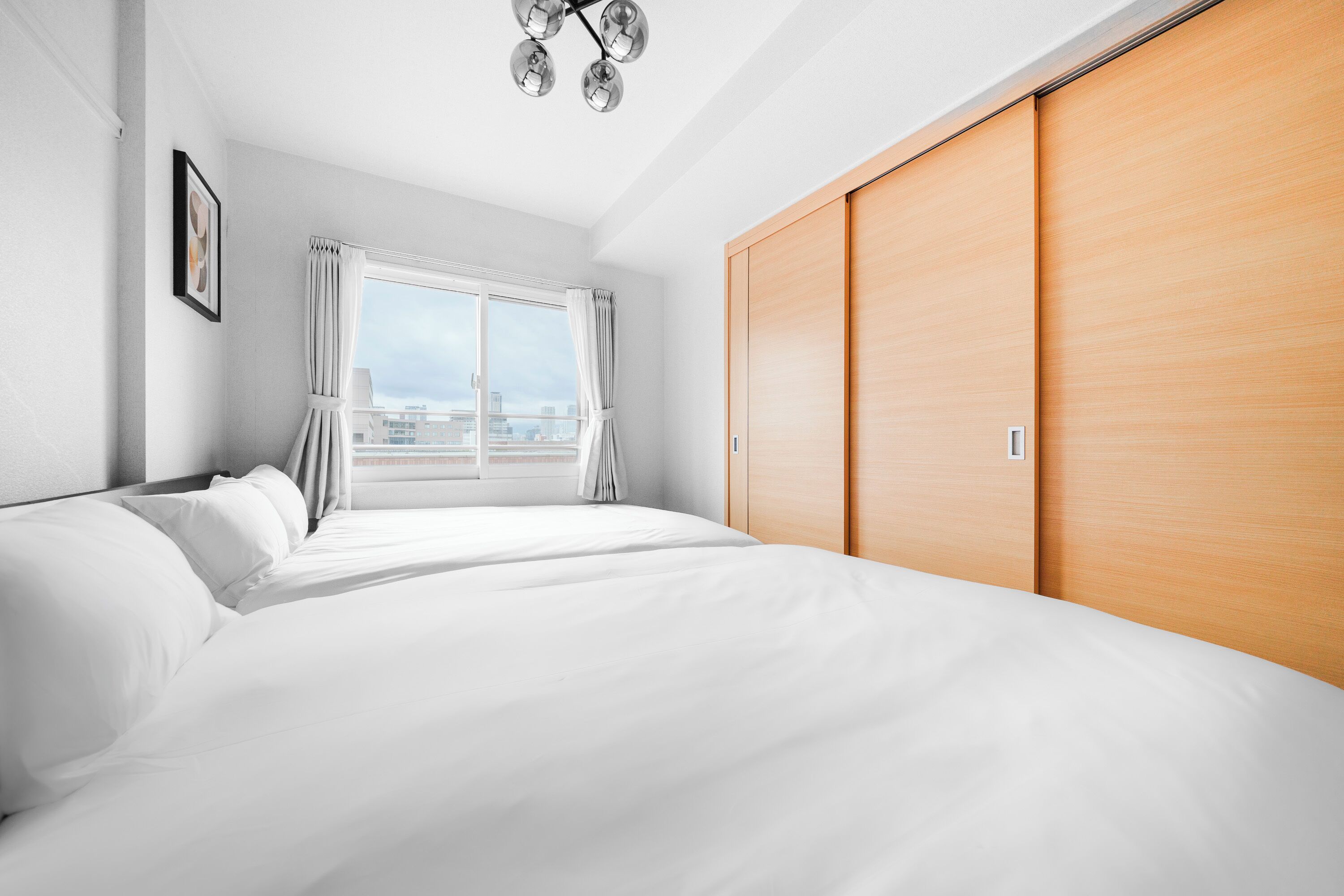 Una habitación de hotel con una cama grande, un armario, una ventana con cortinas y una lámpara en el techo.