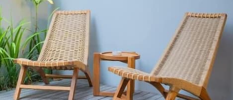Two wicker lounge chairs with a small table on a wooden deck by a pool.