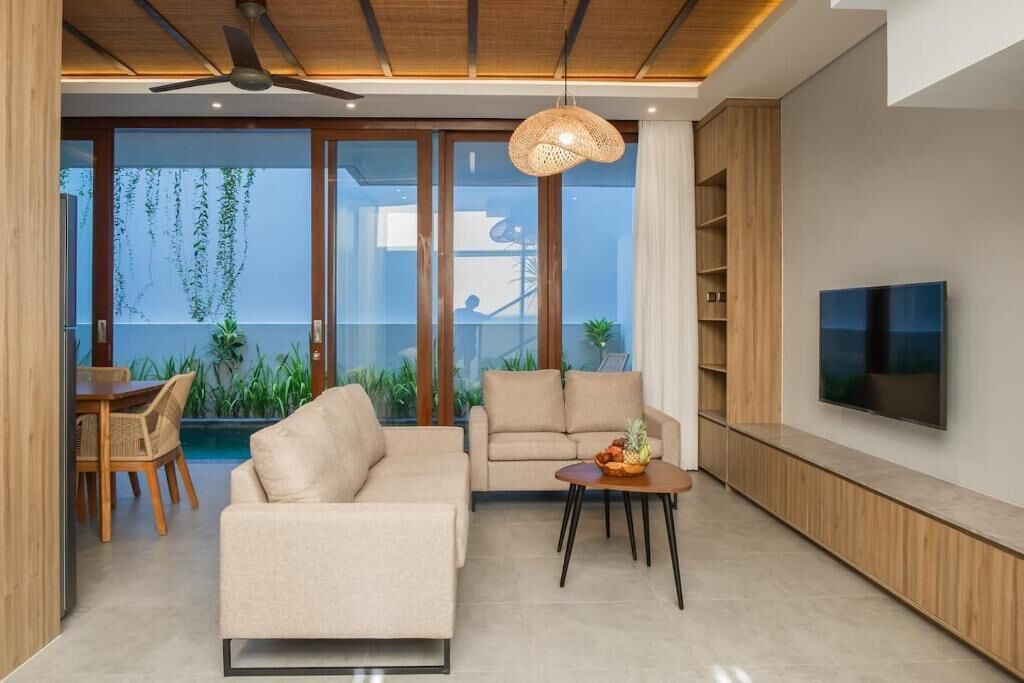 Un salon moderne avec un canapé, un coin repas avec des chaises, un téléviseur fixé au mur et un ventilateur de plafond.