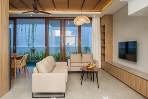 A modern living room with a sofa, a dining area with chairs, a TV on the wall, and a ceiling fan. - Solaris Canggu Villa by Tasvan (Badung)