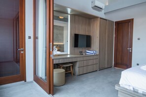 Een moderne slaapkamer met een groot bed, een houten garderobe, een flatscreen televisie en een klein krukje.