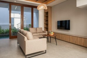 A modern living room with a sofa, a coffee table, a TV, and a wicker pendant light. - Solaris Canggu Villa by Tasvan (Badung)