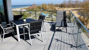 Ein Balkon mit Gartenmöbeln, Blick auf das Meer und eine angelegte Grünfläche.