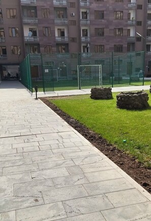 Un vialetto lastricato con un'area verde e elementi in pietra, che conduce a un'area sportiva recintata con un palo della porta.