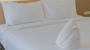 A neatly made bed with white linens and pillows, a wooden headboard, and a bedside table with a lamp. - PT Residence Chonburi (Mueang Chon Buri)