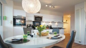 A modern kitchen with white cabinets, a built-in oven, and a dining area with a round table and chairs. - Holiday apartment with 1 bedroom (Heiligenhafen)