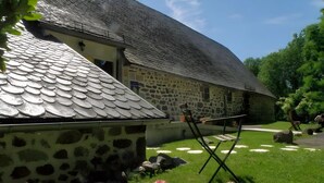 Un edificio de piedra con techo de tejas, un césped con flores y una silla plegable.