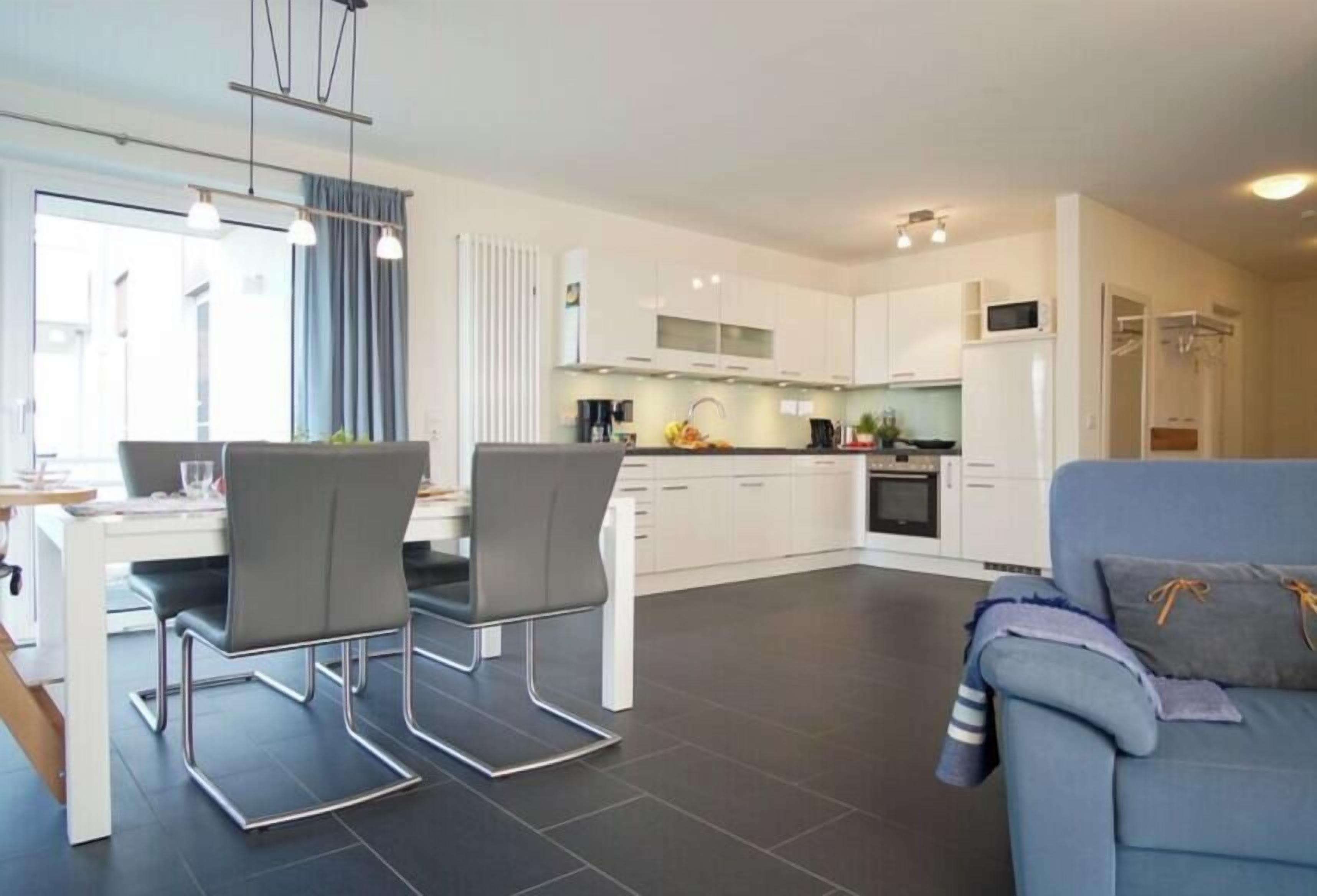 A modern kitchen with white cabinets, a dining area with a table and chairs, and a living area with a sofa.