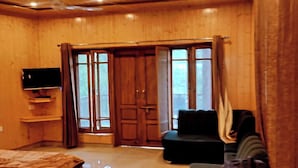 A room with a bed, a television, a sofa, and a sliding door leading to an outdoor area. - The Veteran House (Haripur)