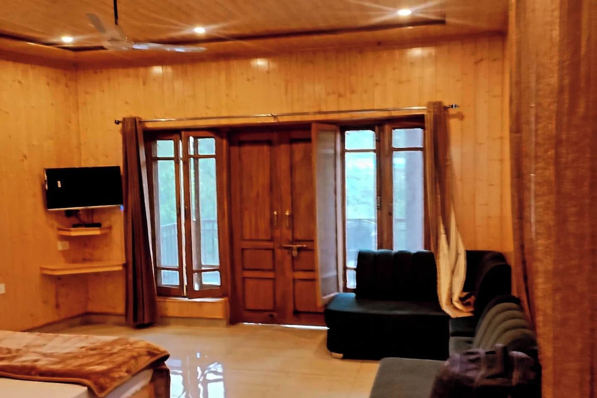 Quarto com cama, televisão, sofá e porta deslizante para área externa.
