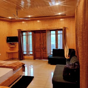 Quarto com cama, televisão, sofá e porta deslizante para área externa.