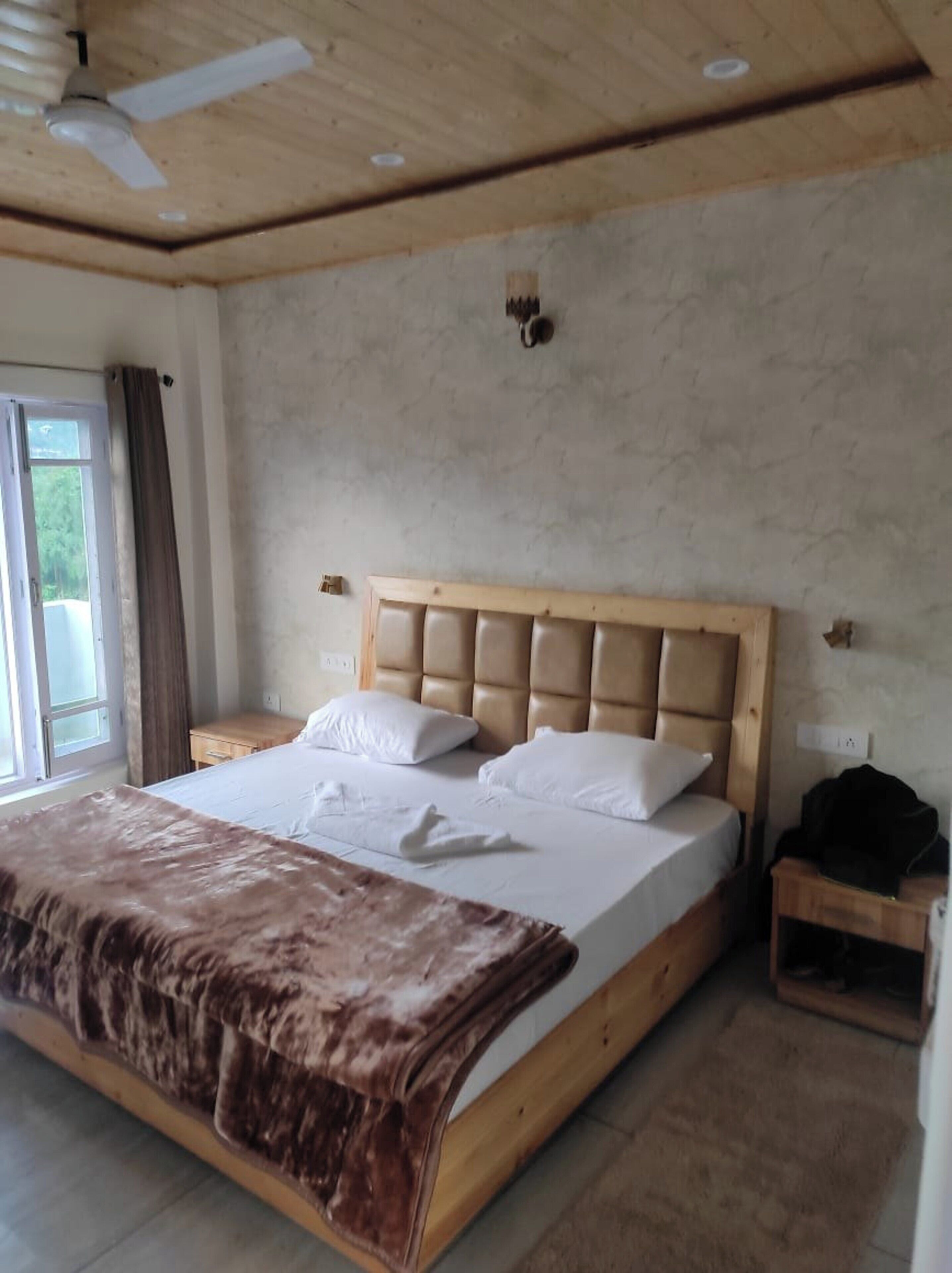 Une chambre à coucher avec un lit, une table de chevet, un ventilateur de plafond et une fenêtre avec des rideaux.