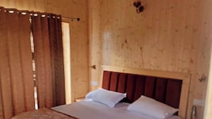 A wooden room with a bed, curtains, and a wooden headboard. - The Veteran House (Haripur)