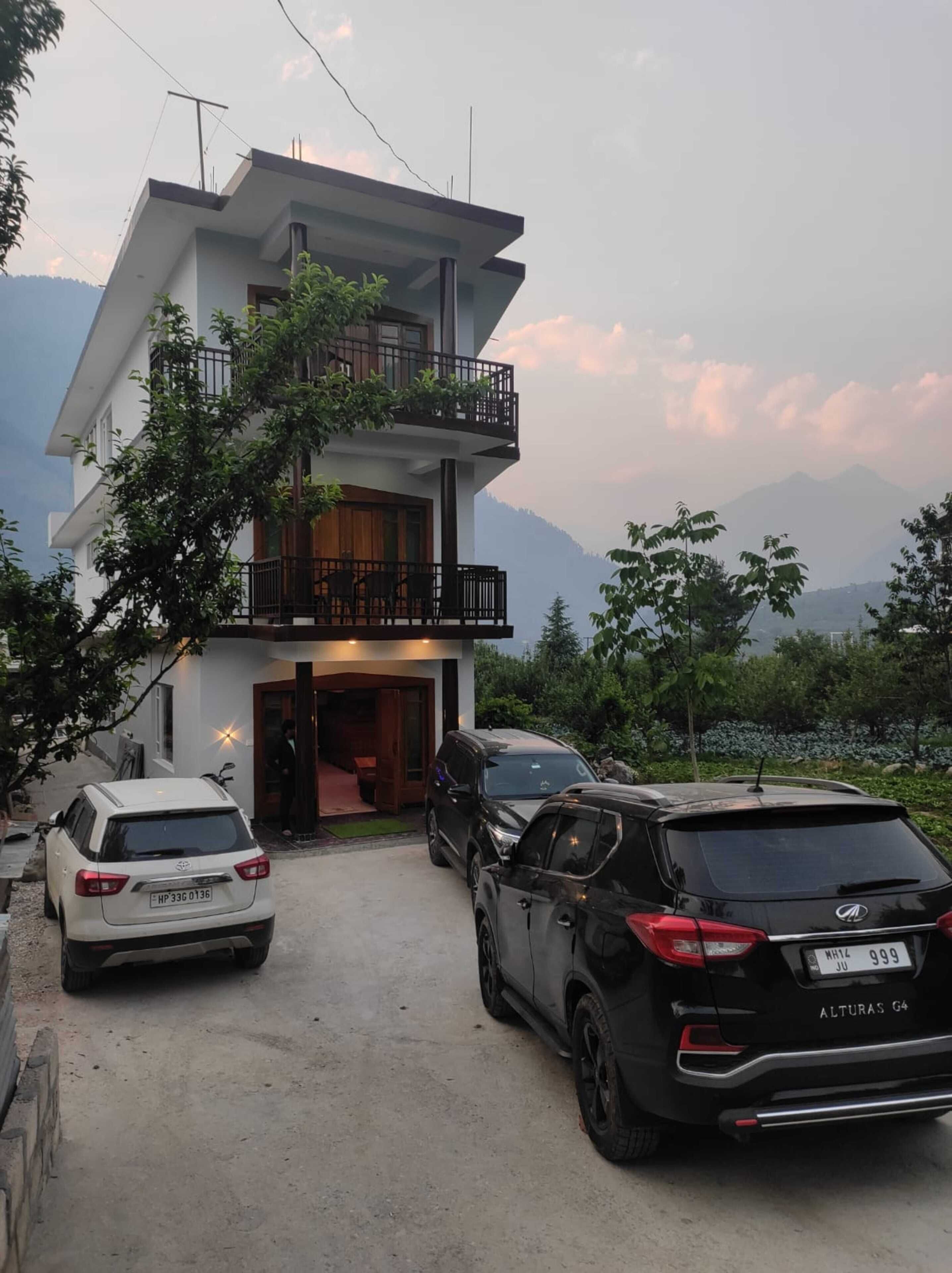 A modern two-story building with a balcony, parked cars, and a mountainous backdrop.