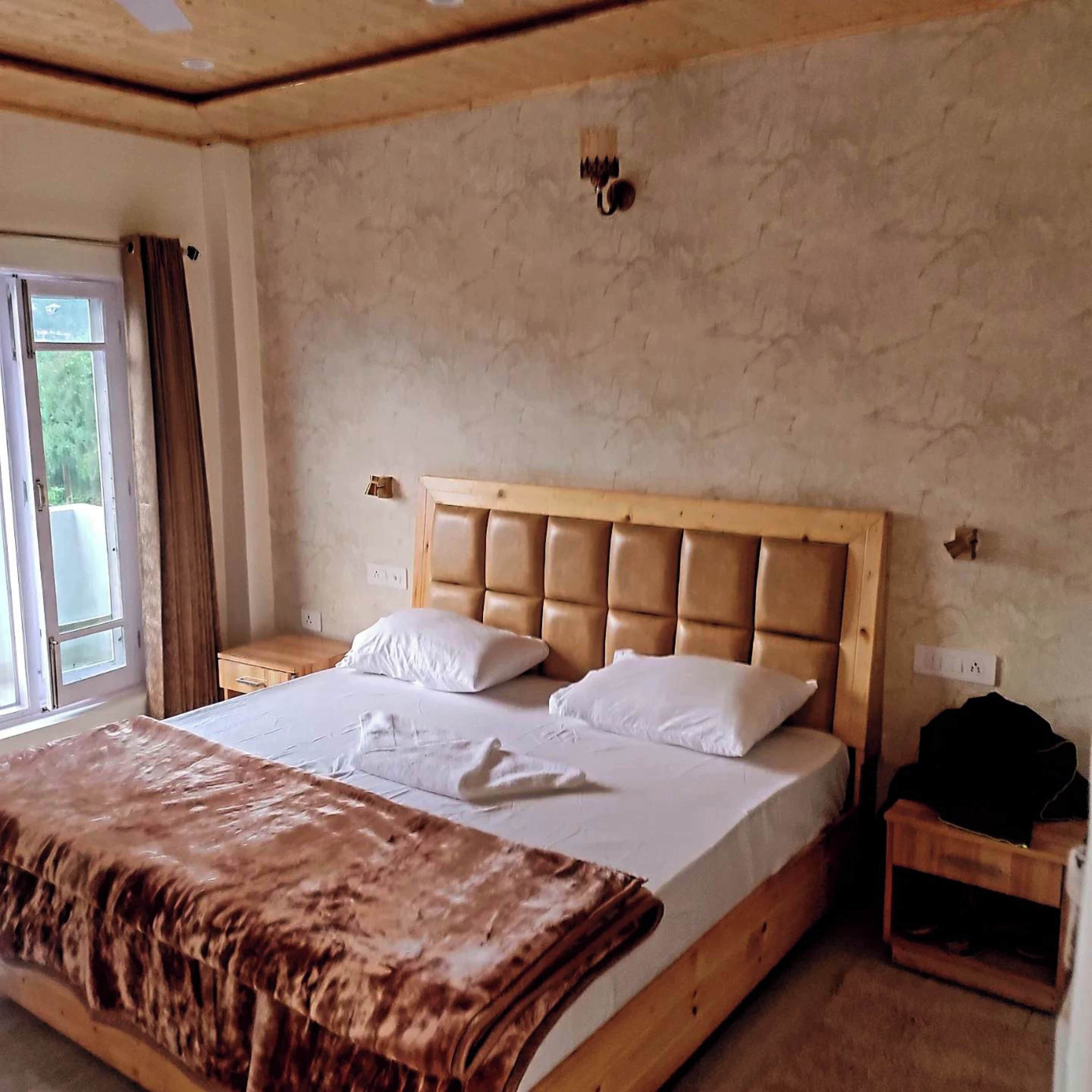 A bedroom with a large bed, a wooden headboard, a bedside table, and a window with curtains.