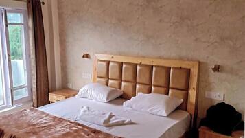 A bedroom with a large bed, a wooden headboard, a bedside table, and a window with curtains.