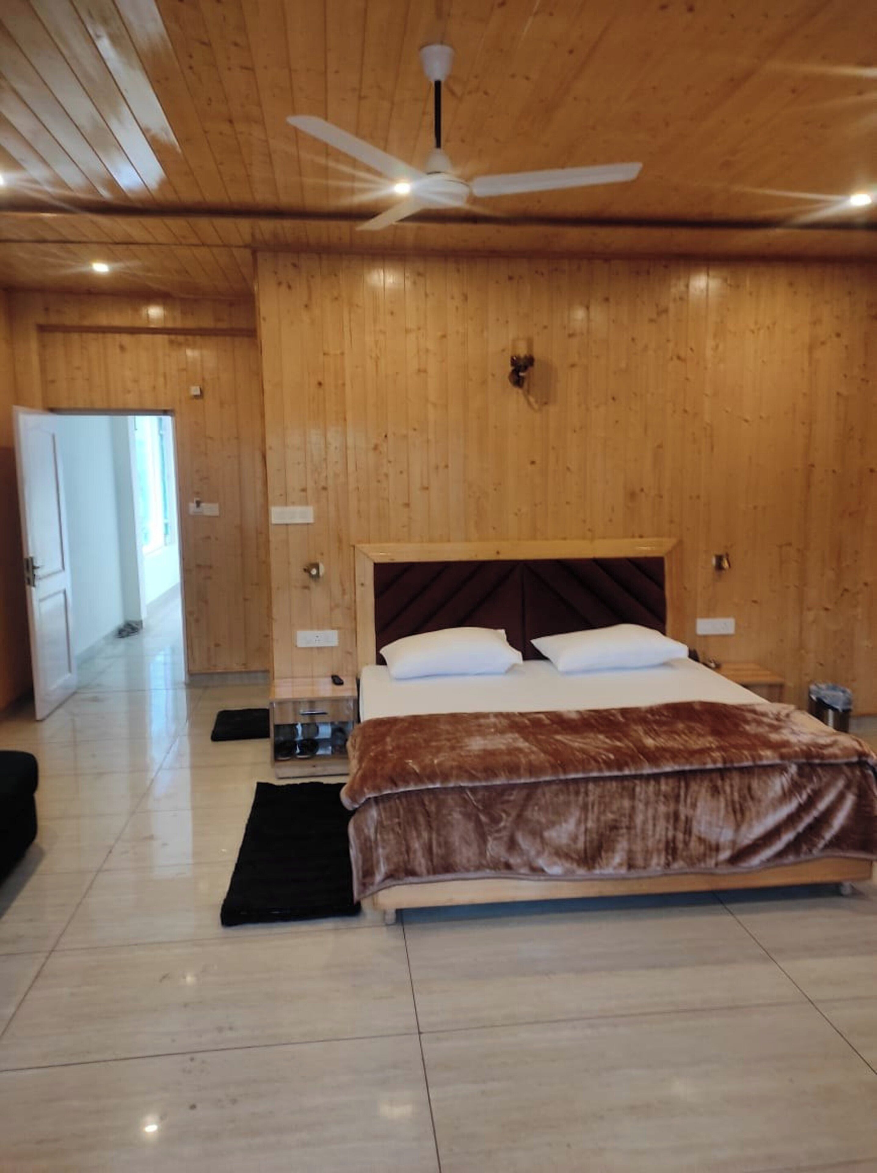 A bedroom with a wooden ceiling, a bed with a brown blanket, a ceiling fan, and a nightstand.