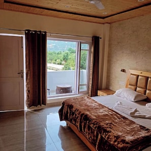 Quarto com cama, janela com cortinas e vista para o verde lá fora, além de teto de madeira.